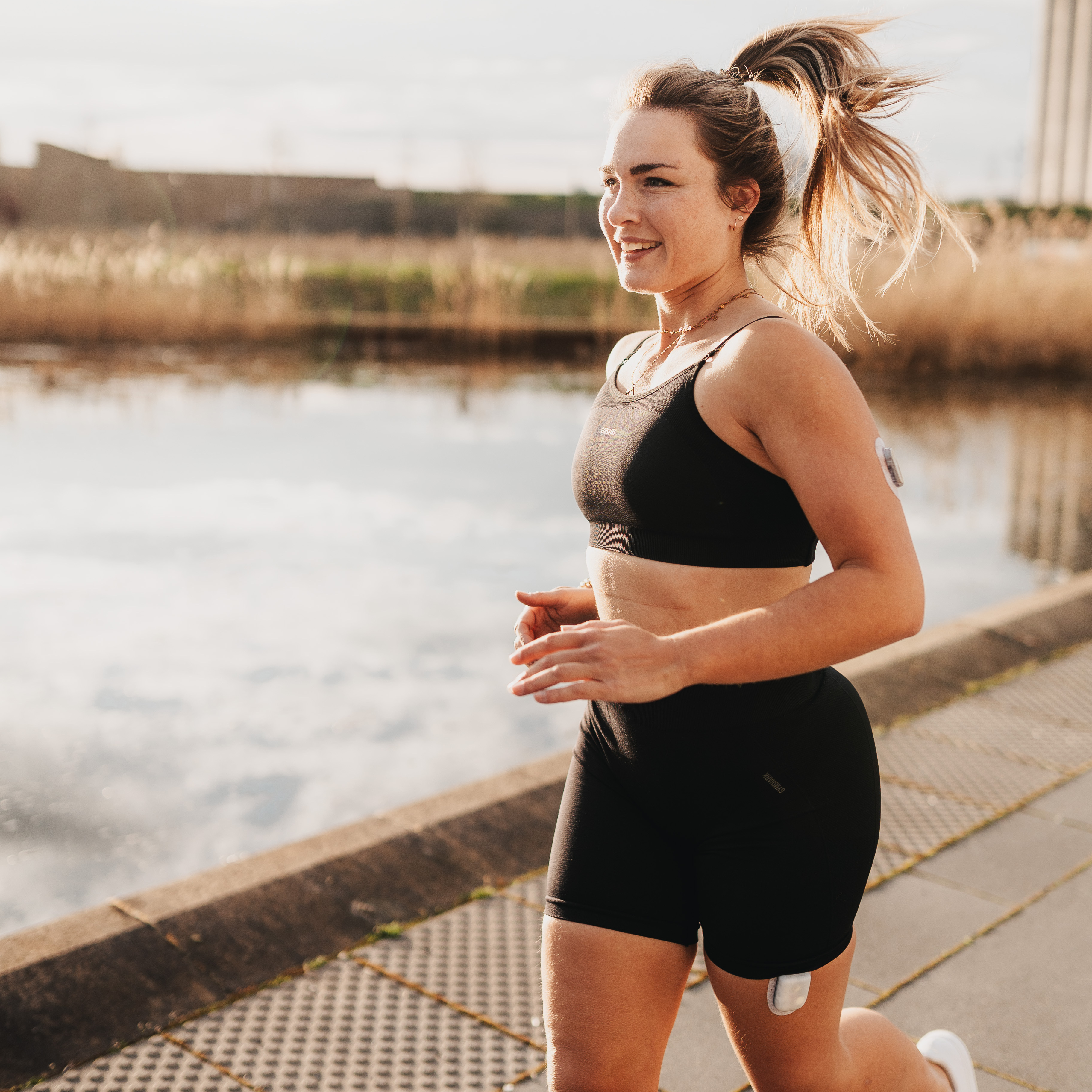 Frau mit Sensor und Insulinpumpe rennt am See entlang