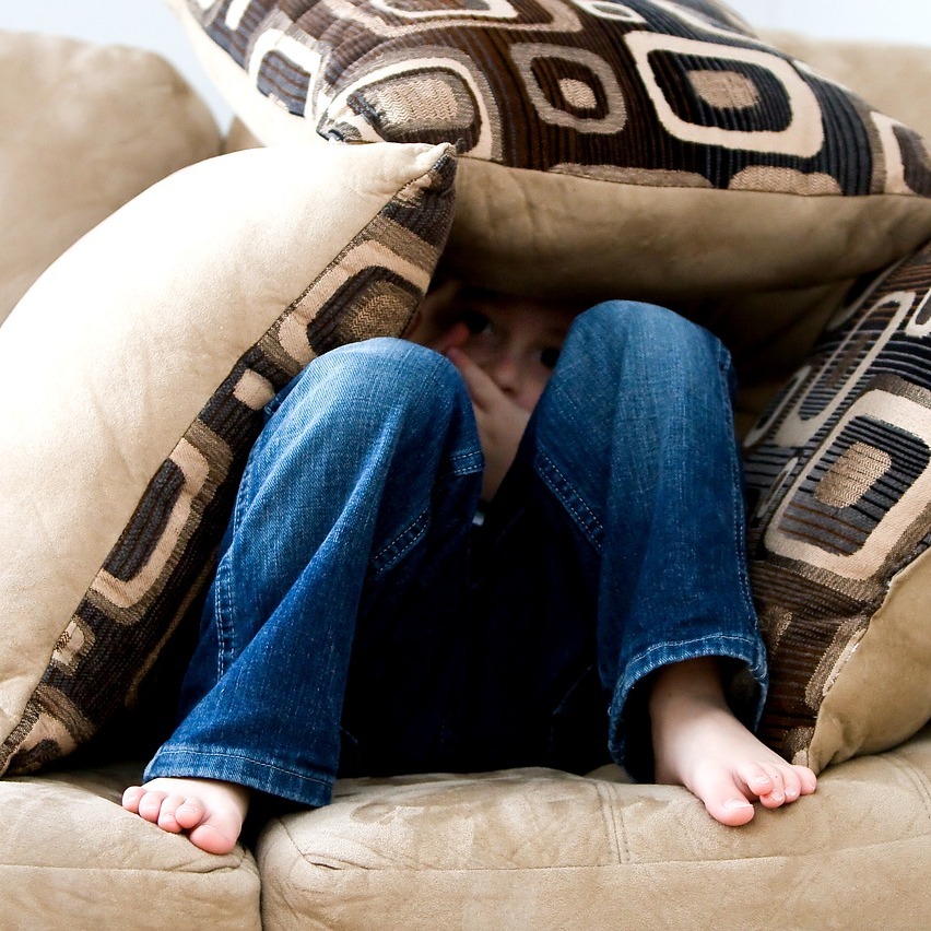 Ein Kind, dass sich auf dem Sofa mit Kissen eine Höhle gebaut hat. 