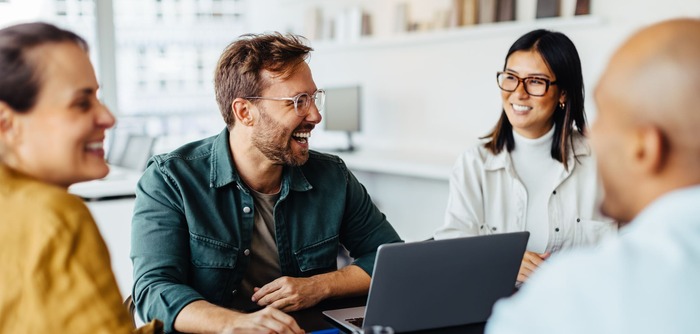 Kolleginnen und Kollegen sitzen zusammen an einem Tisch und sind fröhlich.