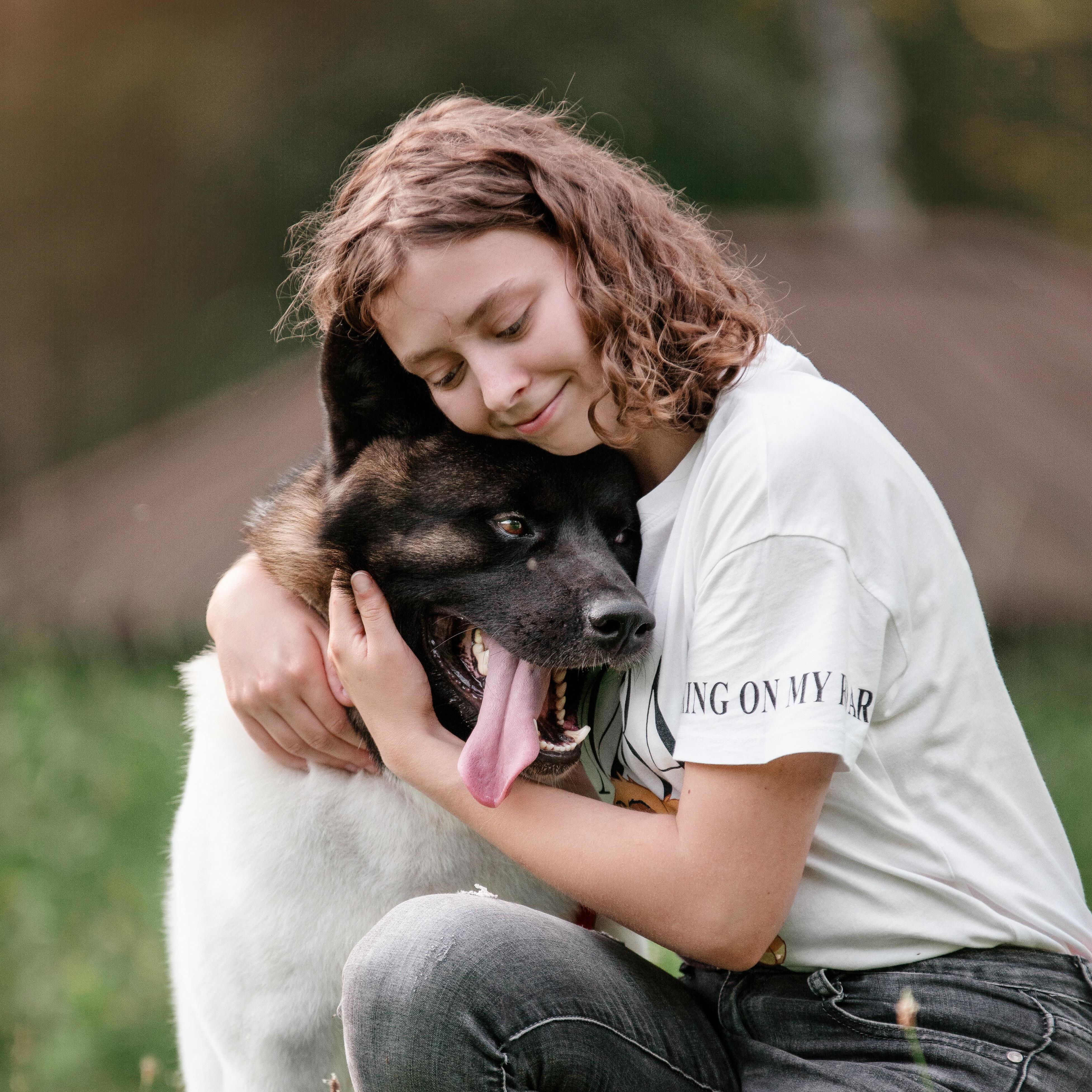 „Eine hochemotionale Nahaufnahme einer jungen Frau mit geschlossenen Augen, die einen großen, dunkel gezeichneten Akita-Hund 
