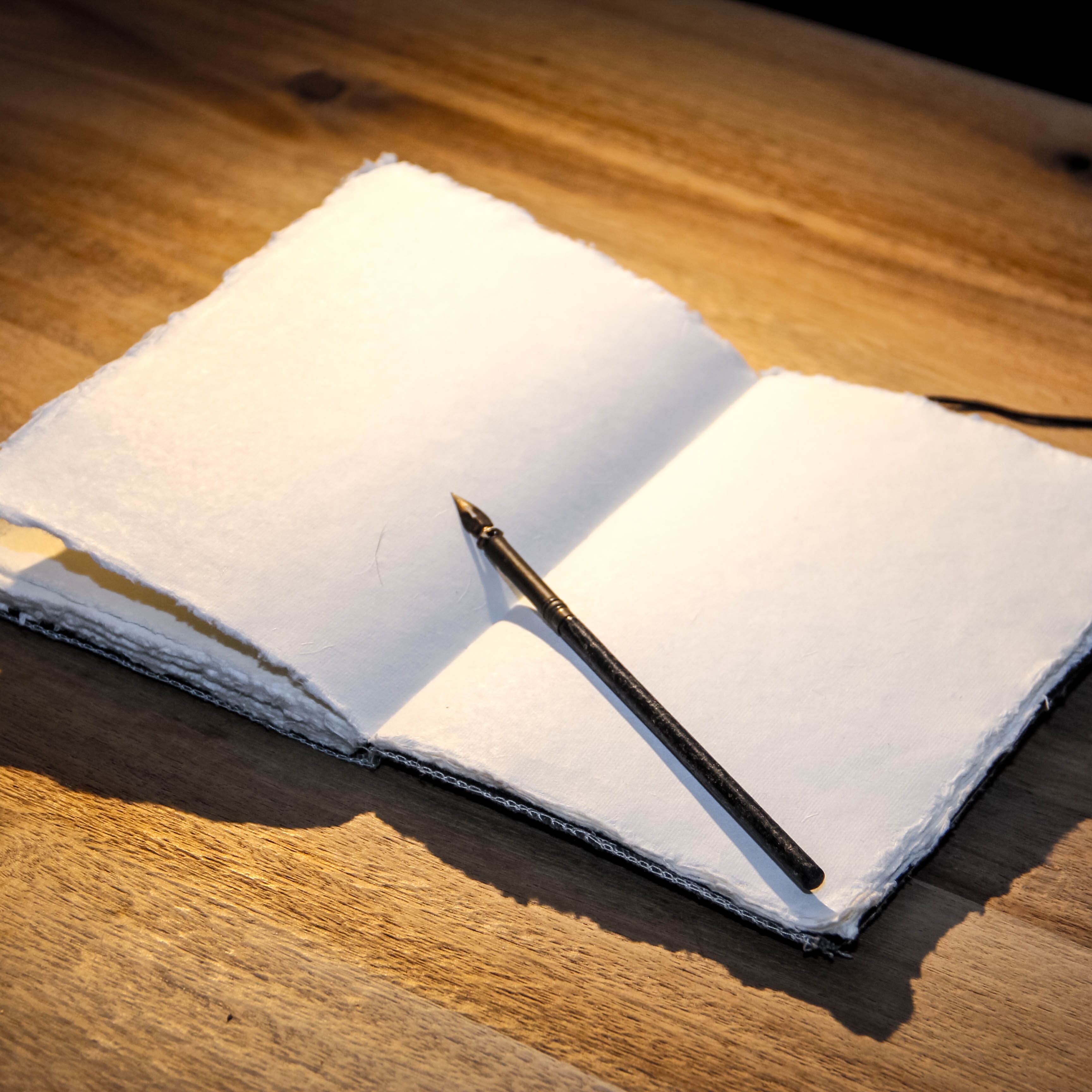 Ein kleines Notzizheft aus selbst geschöpften Papier auf einem Holztisch. Auf dem Notizheft liegt ein alter Füller.