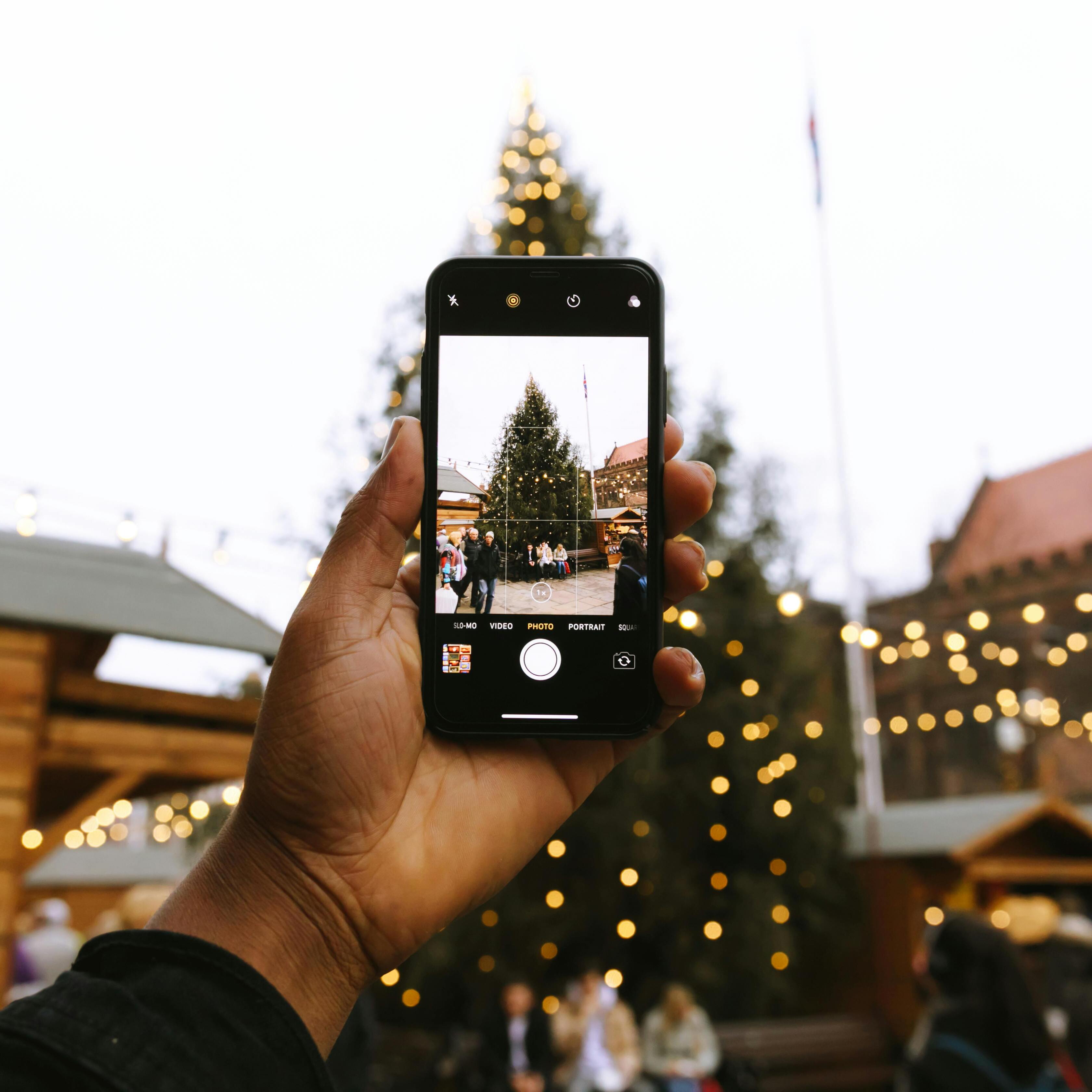 Hand macht Foto mit Smartphone vom Tannenbaum auf dem Weihnachtsmarkt