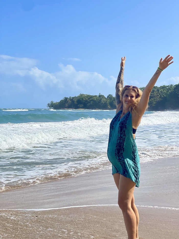 Schwangere Frau steht am Strand und hat die Arme in Freude erhoben