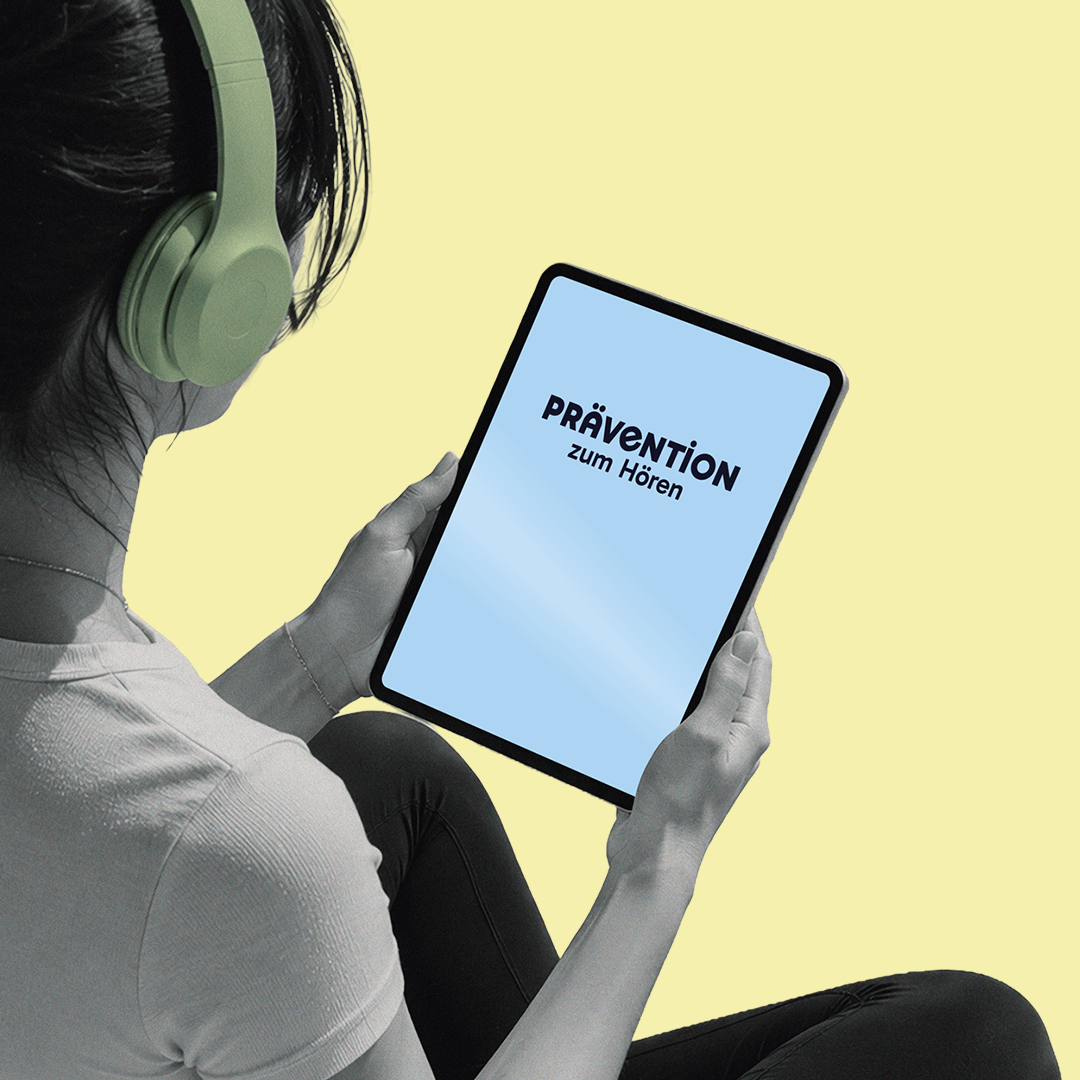 Frau sitzt im Schneidersitz mit Kopfhörern und schaut auf ein Tablet, auf dem „Prävention zum Hören" zu lesen ist.